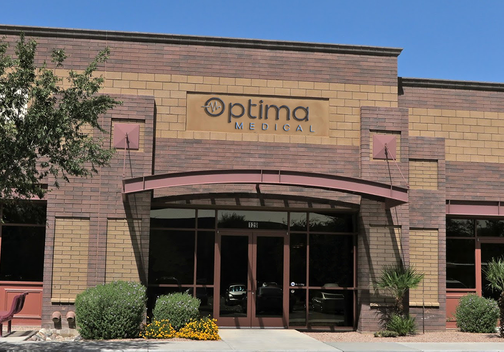 Optima Medical primary care clinic in Mesa, Arizona, featuring a modern brick building with glass entry doors, landscaped frontage, and clear Optima Medical signage.