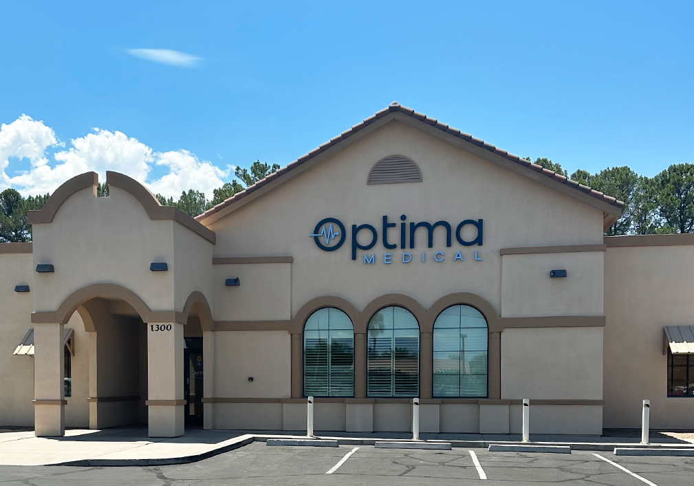 Exterior view of Optima Medical primary care clinic at 1300 South 20th Avenue in Safford, Arizona, featuring tan stucco building with arched windows and blue signage.