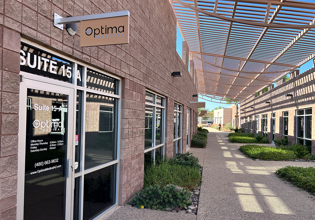 Exterior of Optima Medical primary care clinic at 26224 N Tatum Boulevard Suite 15A in Phoenix, Arizona, featuring modern brick building with glass entrance and clinic signage.