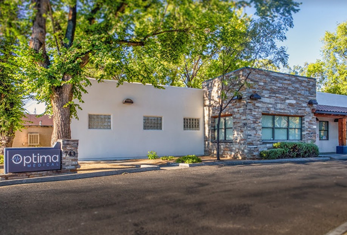 Exterior view of Optima Medical primary care clinic at 743 Miller Valley Road in Prescott, Arizona, surrounded by trees and parking area.
