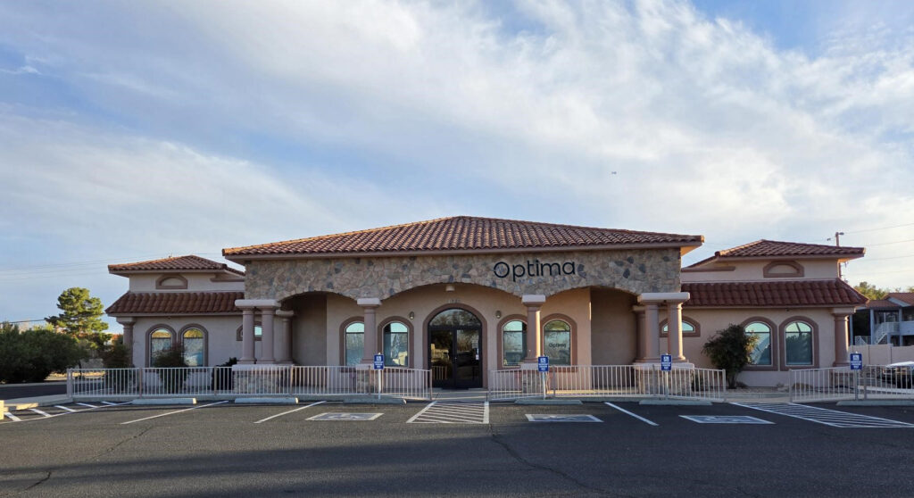 Optima Medical primary care clinic in East Sierra Vista, Arizona, featuring a tan building with stone accents, red tile roof, and arched entrances under a clear sky.