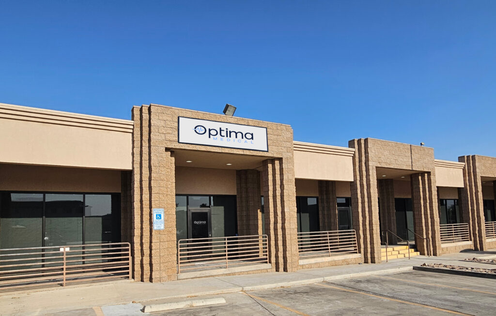 Optima Medical primary care clinic in Central Lake Havasu, Arizona, featuring a tan modern building with columned entrance and accessible front ramp under clear blue skies.